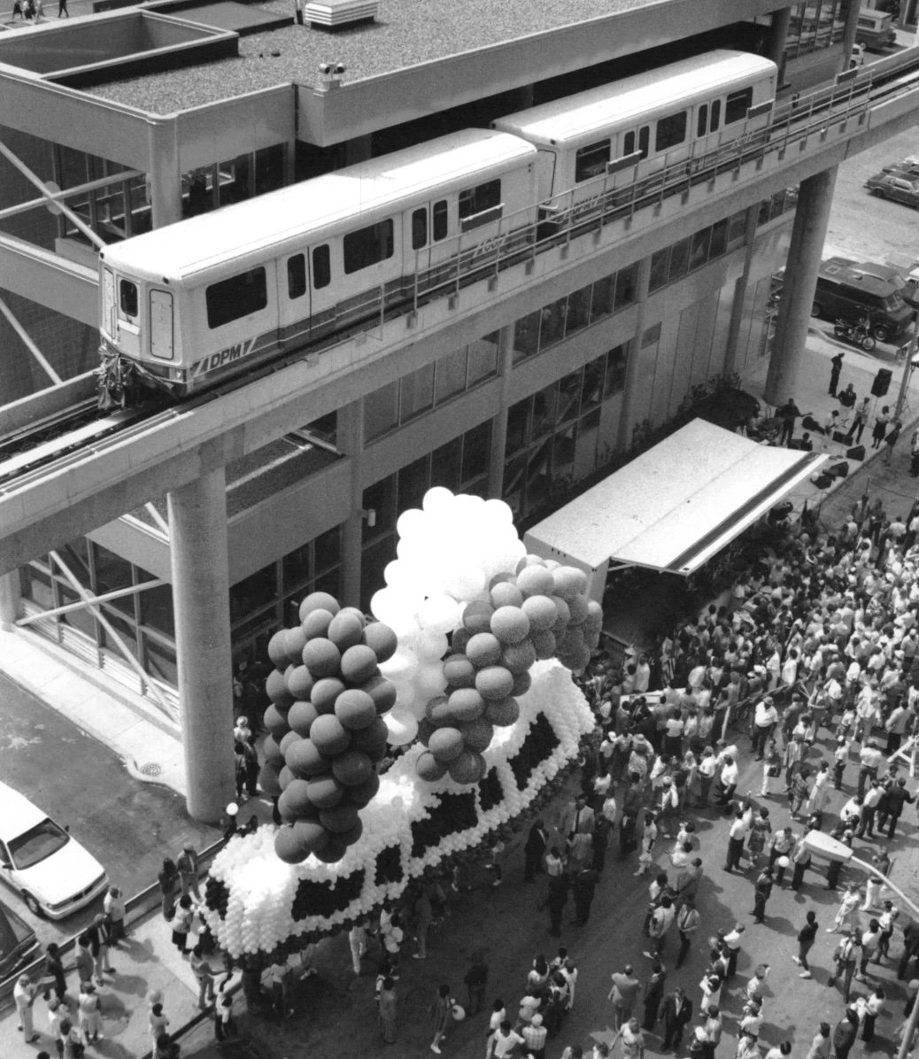 Archival photograph of a People Mover train above a downtown crowd and a large balloon sculpture